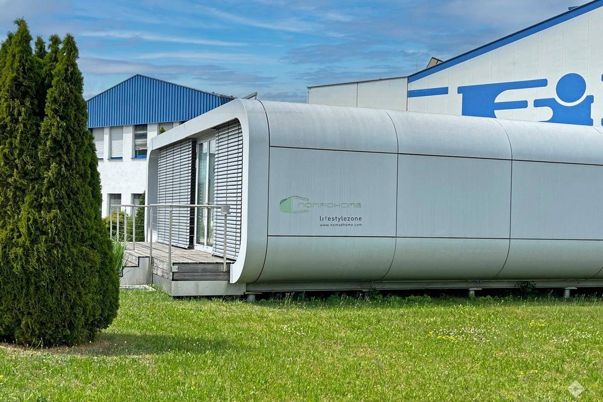 Moderne, modulare Gebäudeeinheit mit abgerundeten Ecken und kleiner Holzterrasse auf einer Grünfläche.
