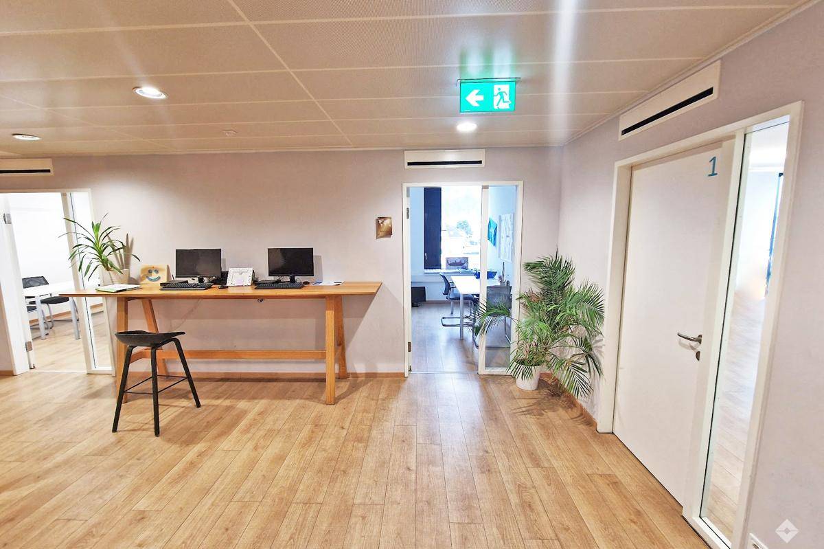 Heller Empfangsbereich mit Holzboden, Arbeitsplätzen und Zugang zu weiteren Büroräumen.