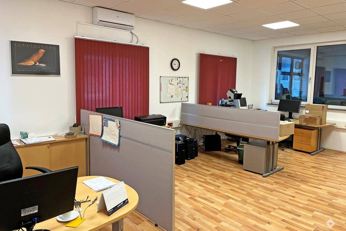 Helles Büro mit mehreren Arbeitsplätzen, Holzfußboden und Klimaanlage an der Decke.