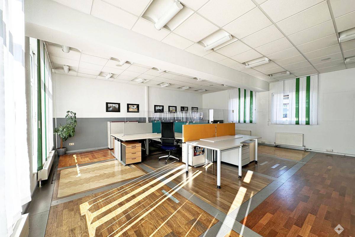 Heller Bürobereich mit Arbeitsplätzen, Holzparkett und grünen Jalousien, gut beleuchtet.