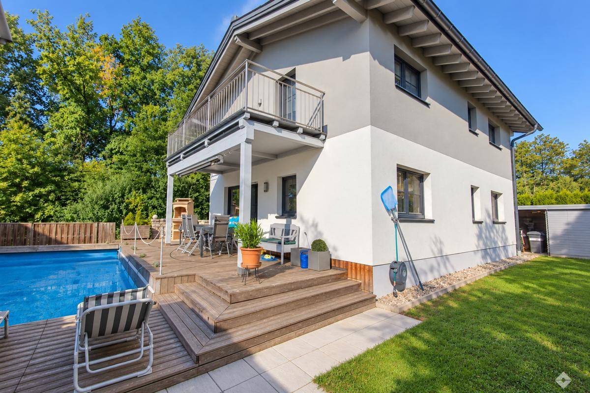 Modernes Haus mit großem Pool, Holzterrasse und möbliertem Außenbereich unter blauem Himmel.