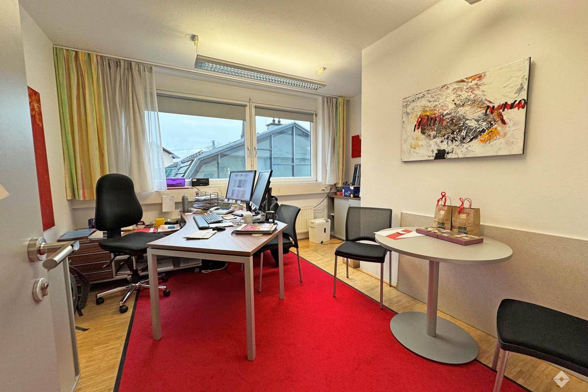 Helles Büro mit rotem Teppich, Schreibtisch und Blick auf die Dächer.