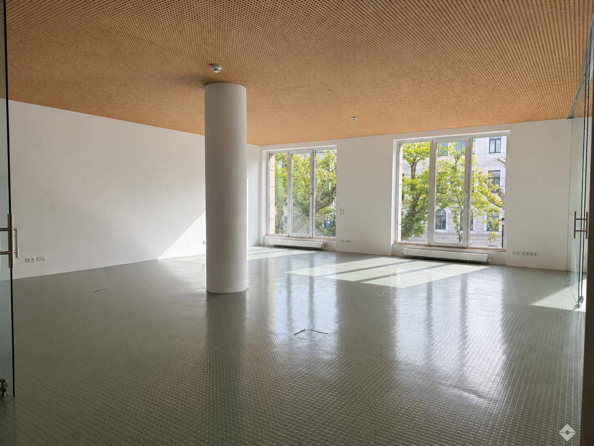 Moderner Büroraum mit Säulen, großen Fenstern und einem perforierten Holzdeckenpaneel.
