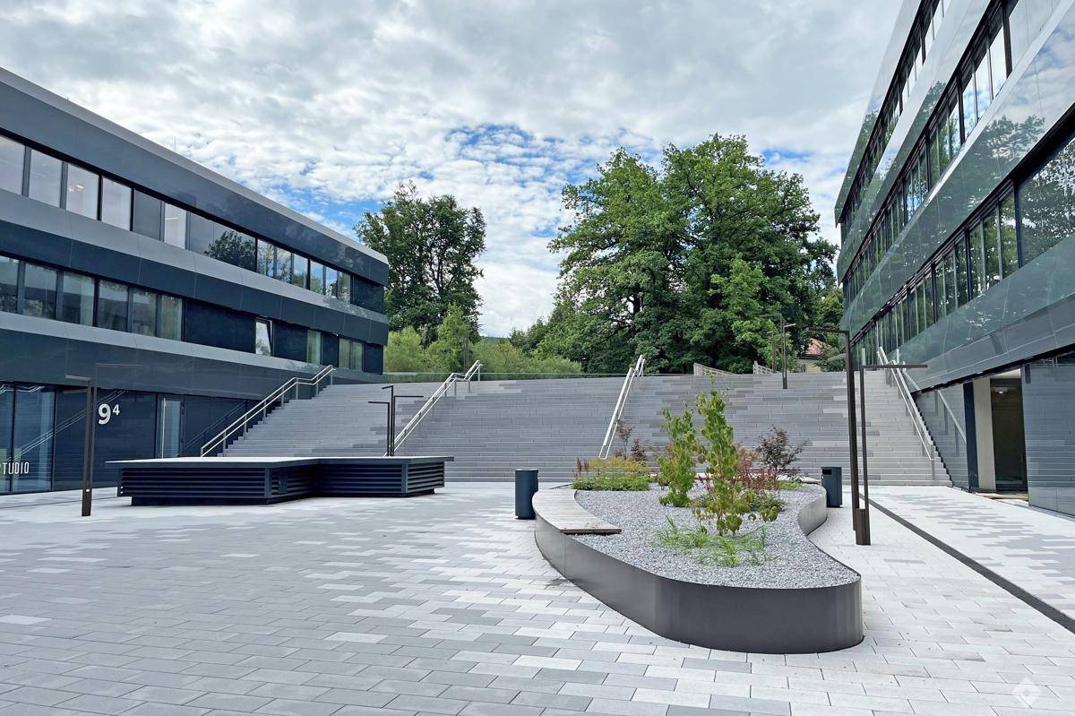 Moderner Außenbereich mit breiter Treppe, gepflastertem Platz und Sitzgelegenheiten zwischen den Bürogebäuden.