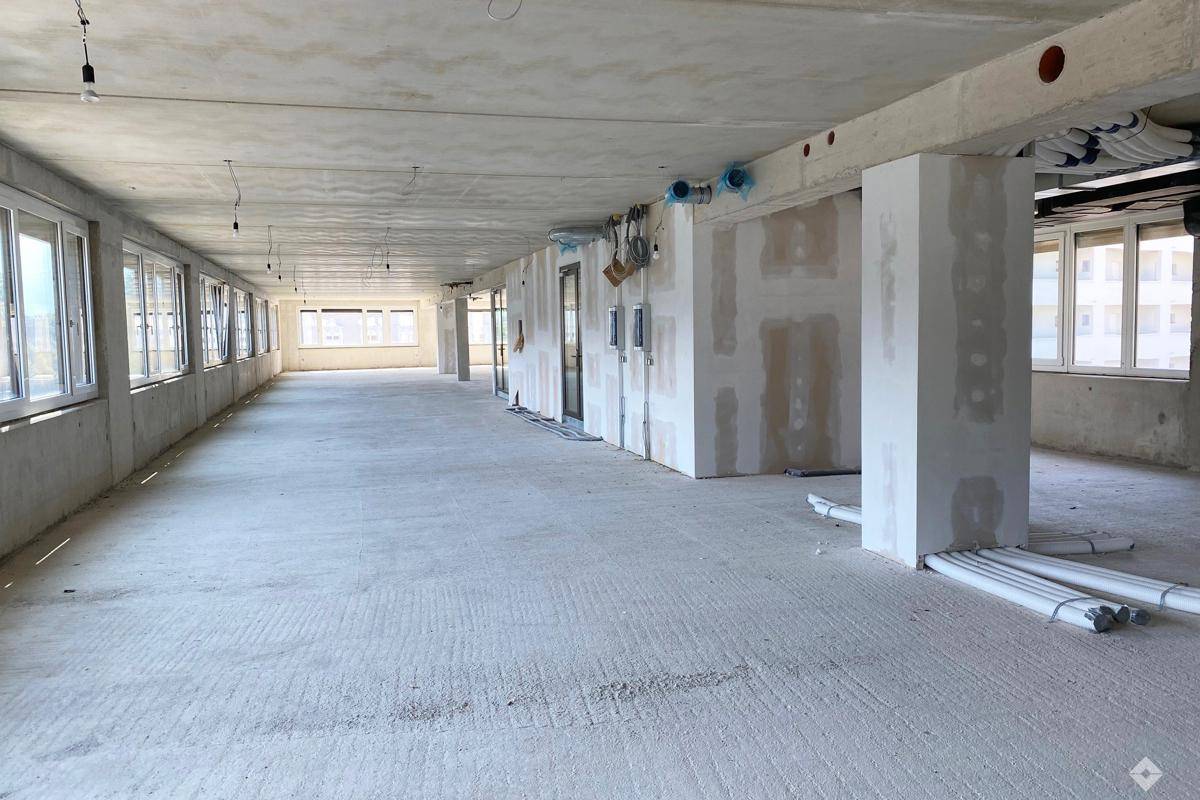 Großer, offener Gewerberaum im Rohbau mit vielen Fenstern, Betonboden und hohen Decken, bereit für den Ausbau.