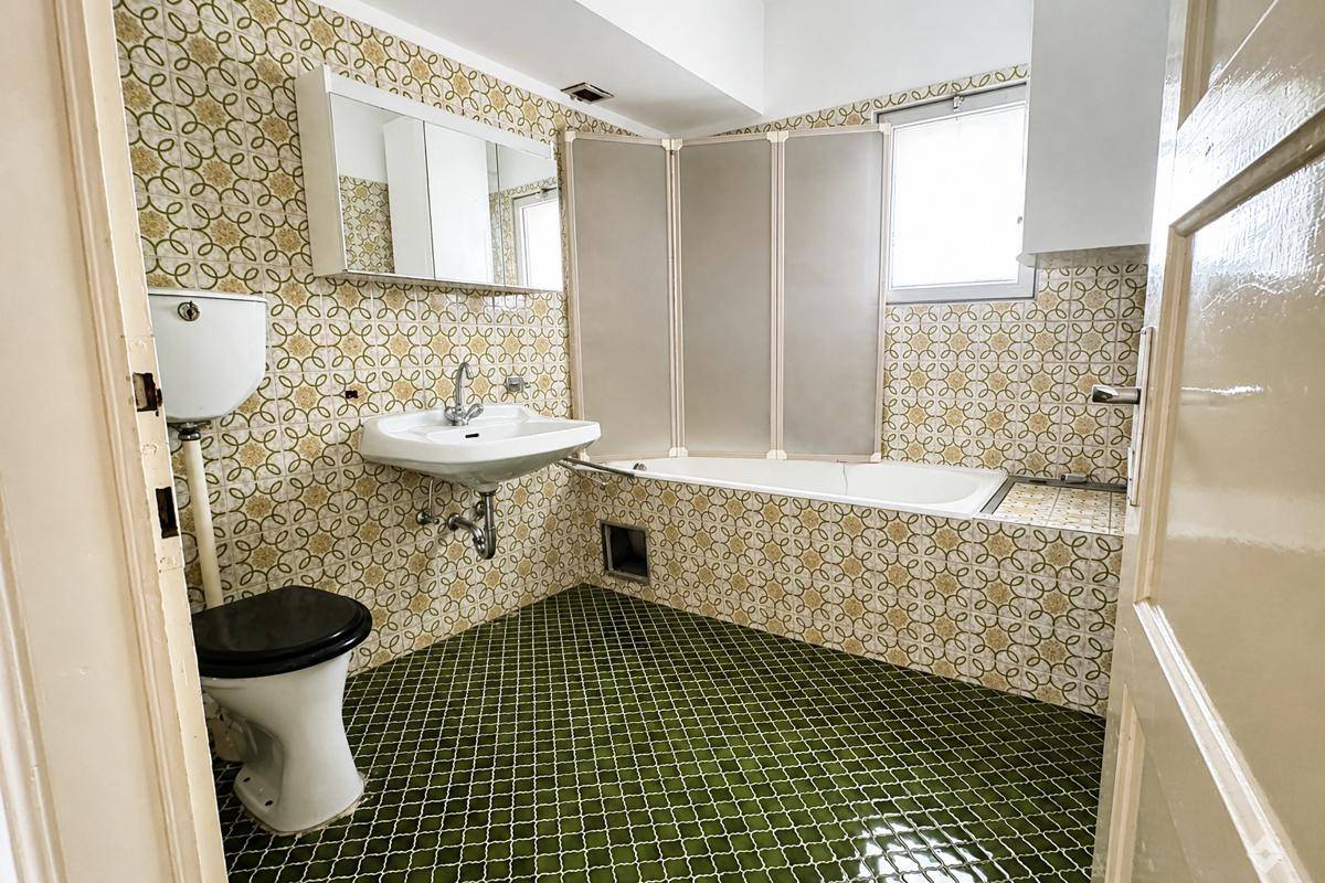 Badezimmer im Stil der 80er Jahre mit gemusterten Fliesen und Badewanne.