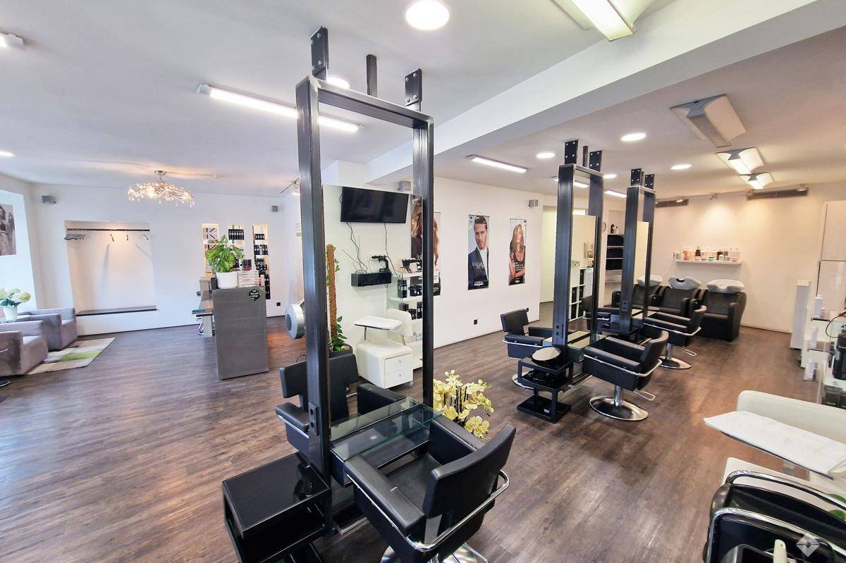 Blick in den Friseursalon mit mehreren Styling-Stationen, großen Spiegeln und dunklem Laminatboden.