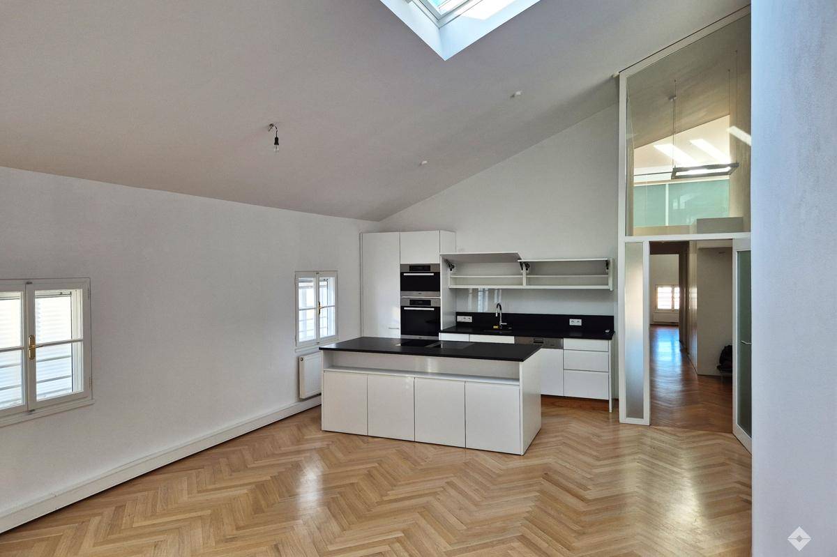 Moderne offene Küche mit Kochinsel, Dachschräge und Fischgrätparkett in einem hellen Raum.