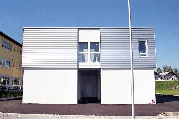 Seitenansicht eines modernen Gebäudes mit horizontaler Verkleidung und großen Fenstern.