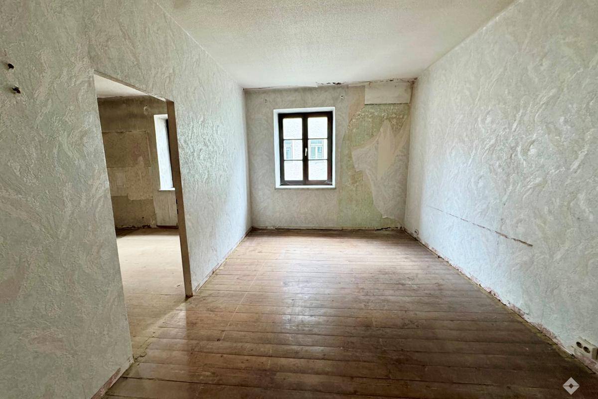 Renovierungsbedürftiger Raum mit alten Tapeten und Holzdielenboden, bietet viel Potenzial.