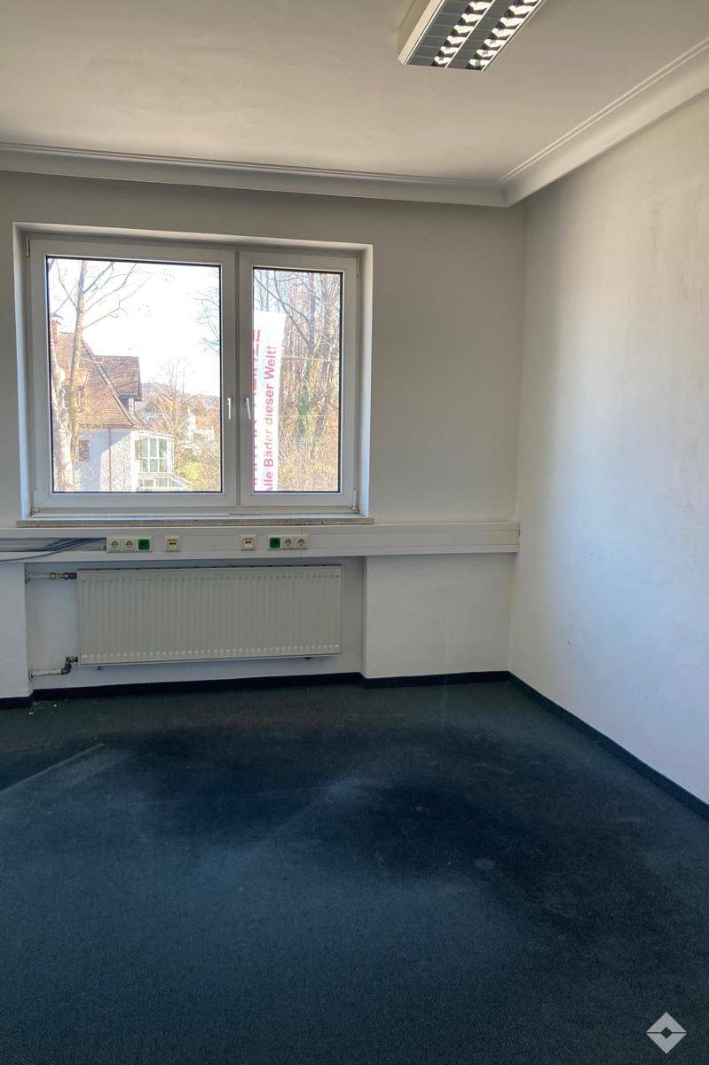 Langer Flur mit Teppichboden, weißen Wänden und mehreren Türen, der zu verschiedenen Büros führt.