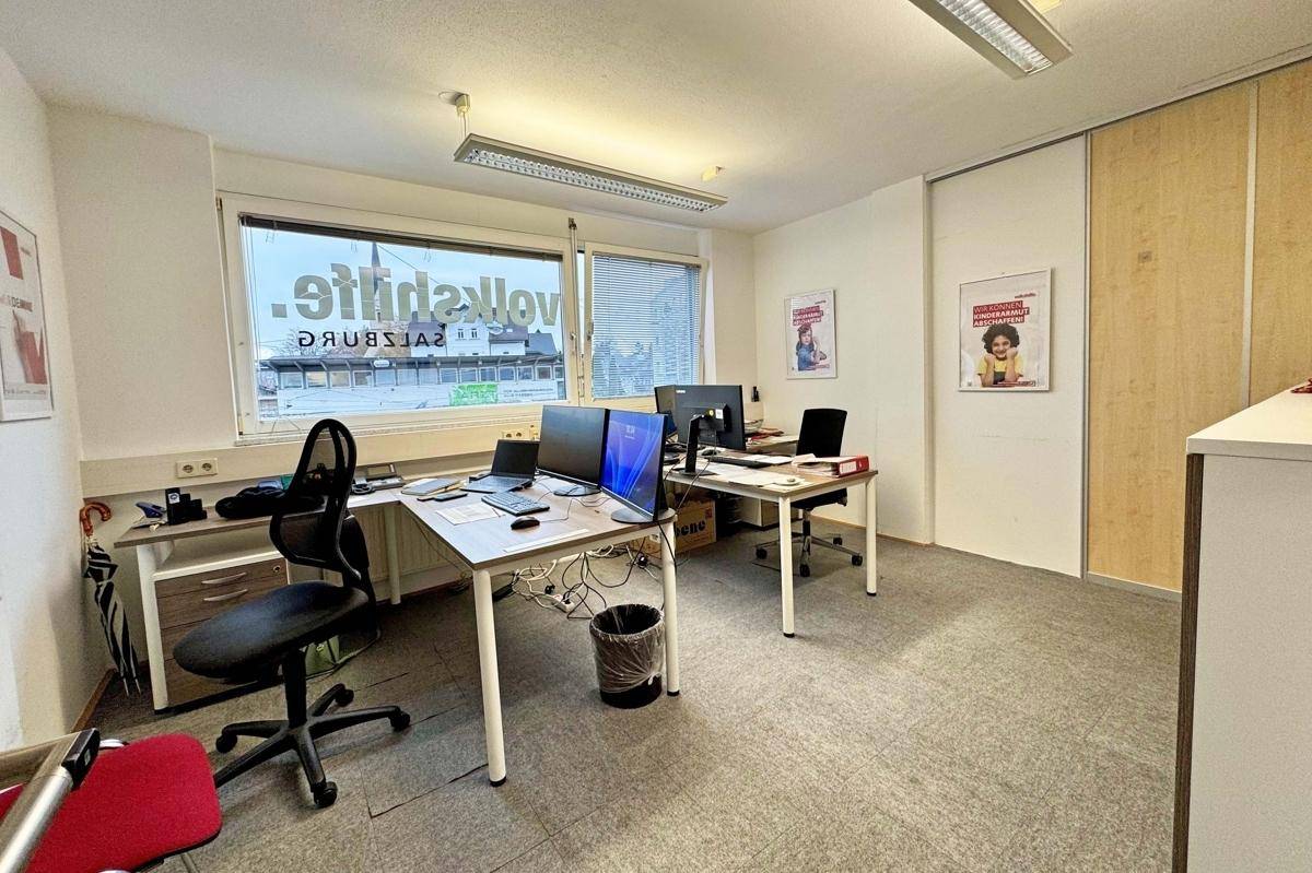 Offenes Büro mit mehreren Arbeitsplätzen, grauem Teppichboden und Blick auf die Straße.