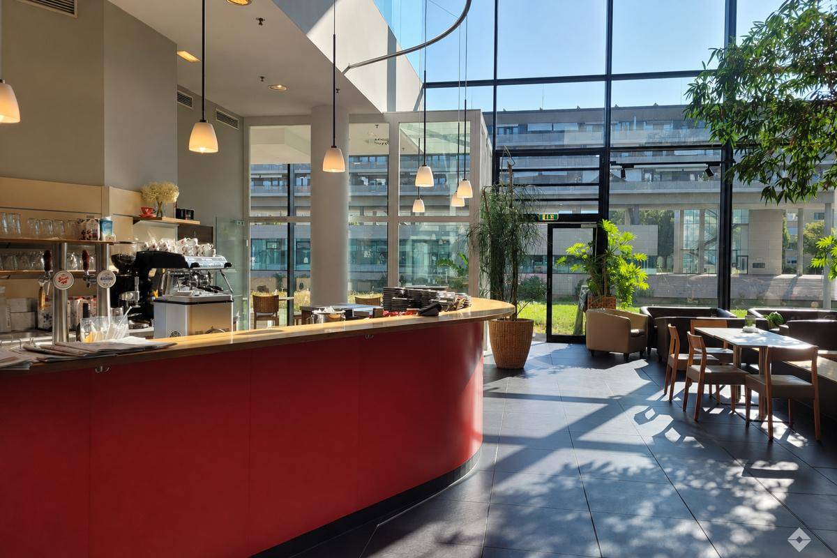 Heller Cafébereich mit roter Theke, großen Glasfronten und Blick ins Grüne.