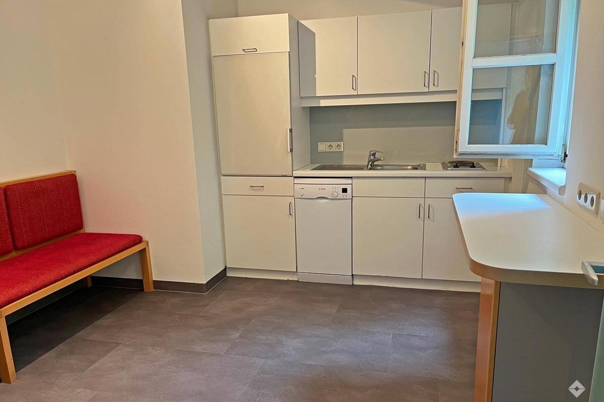 Kleine Küchenzeile mit weißen Schränken, Kühlschrank, Geschirrspüler und einem Fenster.