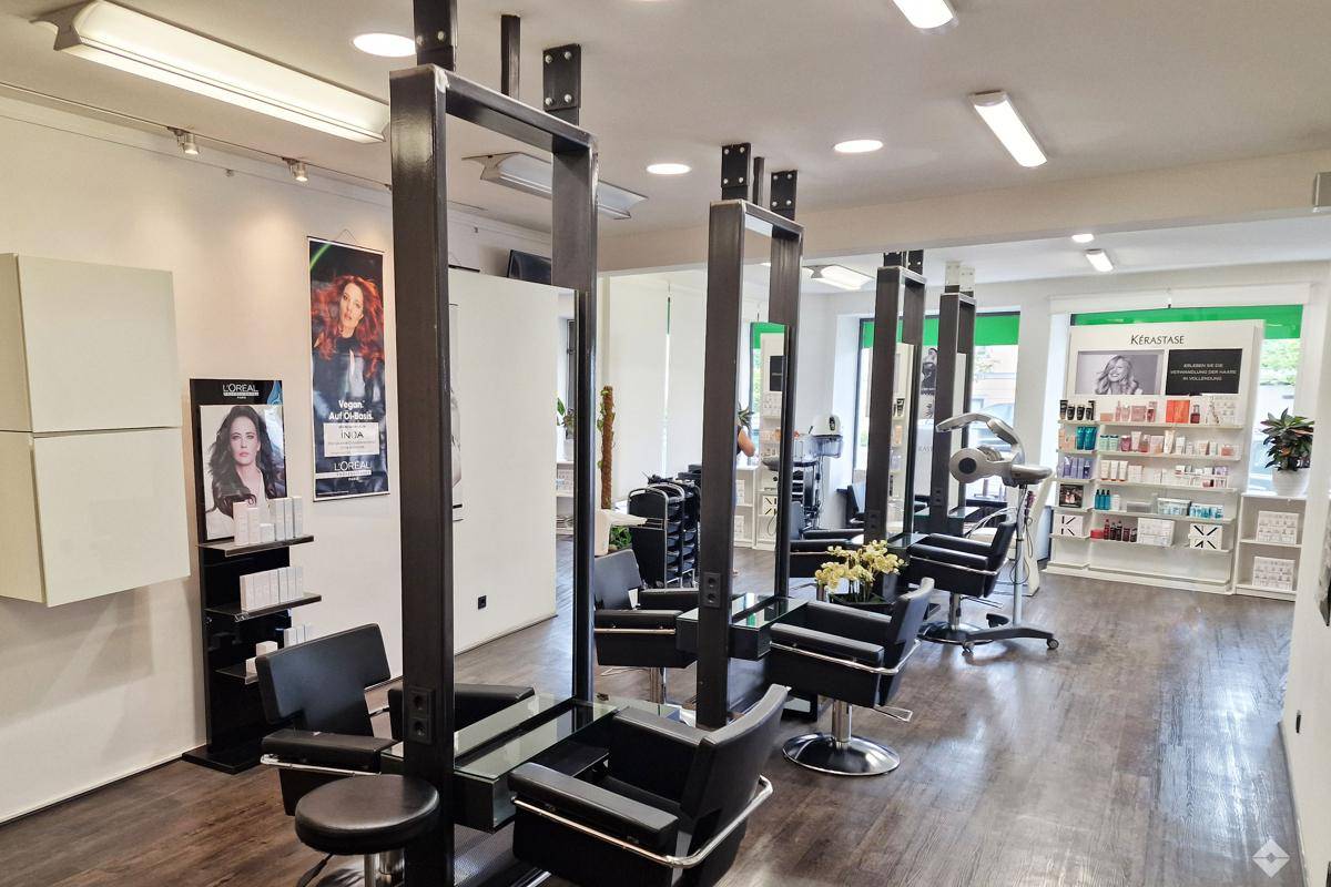 Friseursalon mit mehreren Bedienplätzen, Produktregalen und Trockenhauben in modernem Ambiente.