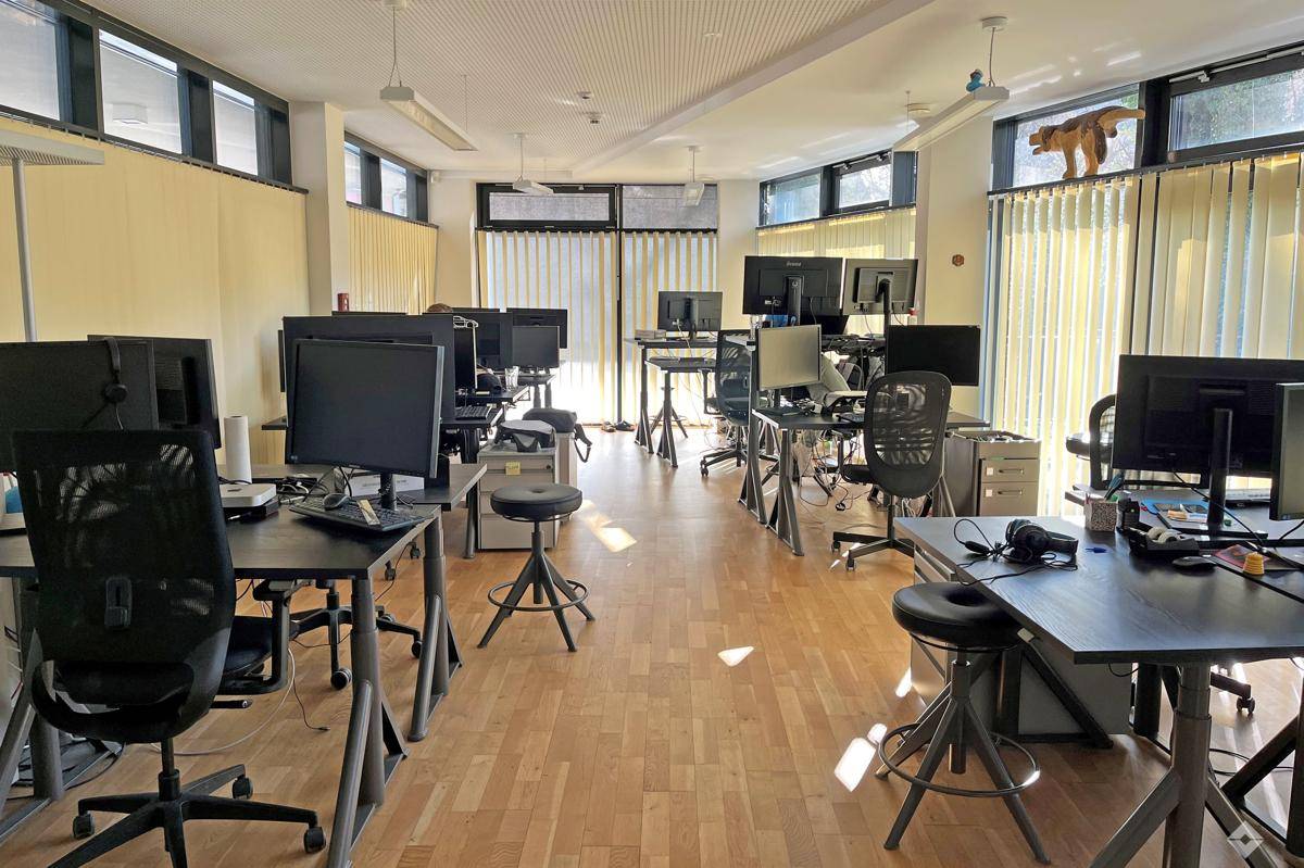 Geräumiges Großraumbüro mit vielen Schreibtischen, ergonomischen Stühlen und hellem Holzfußboden.