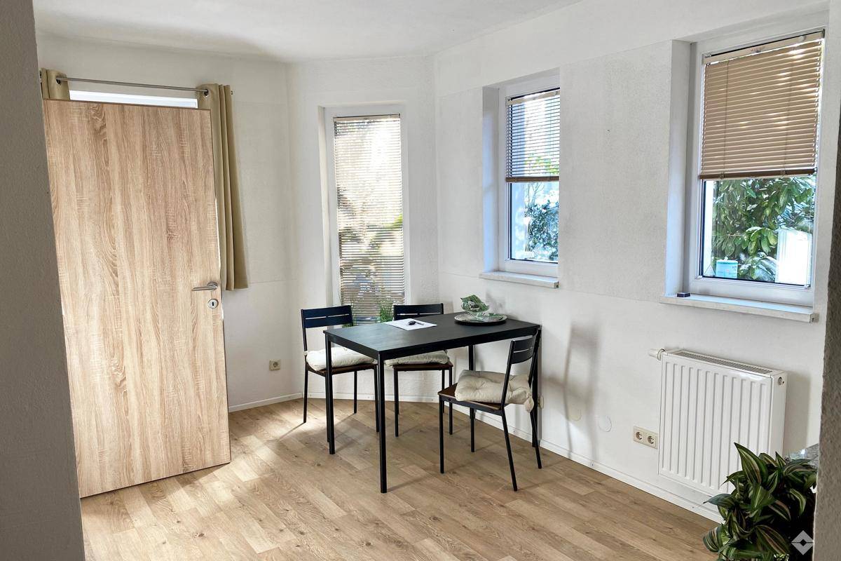 Essbereich mit Holzboden, drei Fenstern und einem kleinen Tisch mit Stühlen.