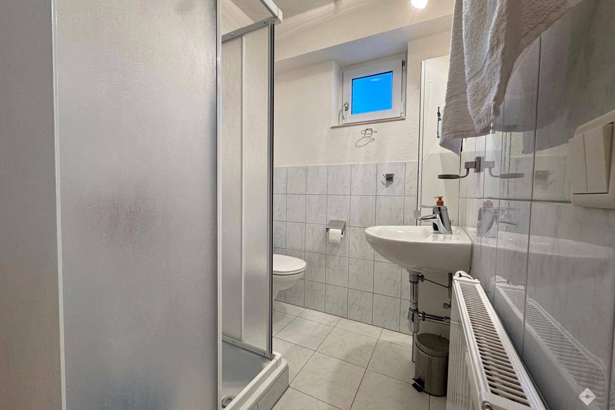 Badezimmer mit Duschkabine, WC, Waschbecken und kleinem Fenster.