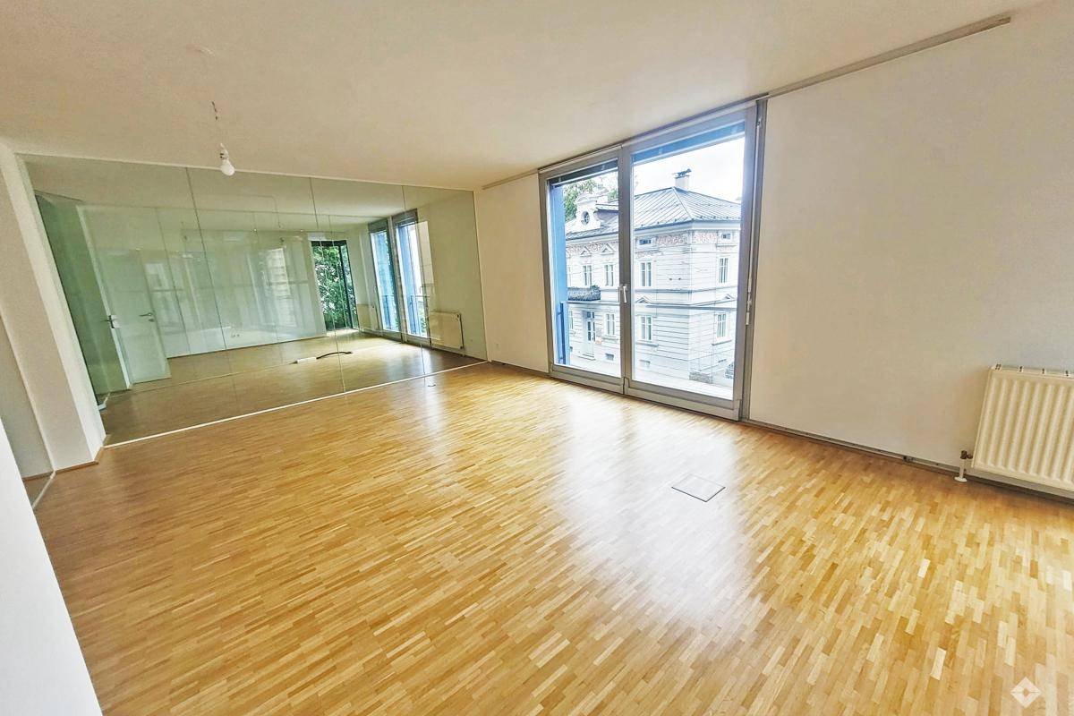 Heller Wohnraum mit Parkettboden, großen Fenstern und Blick auf die umliegenden Gebäude.
