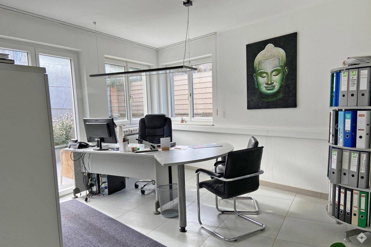 Funktionales Büro mit Schreibtisch, Bürostühlen, Aktenschränken und einem Fenster mit Blick nach draußen.