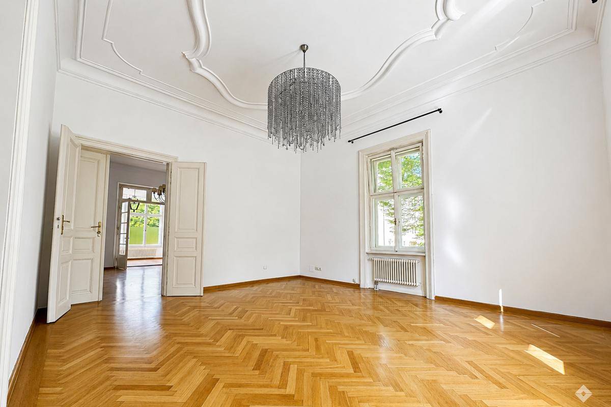 Eleganter Wohnraum mit aufwendiger Stuckdecke, Fischgrätparkett und einem modernen Kronleuchter.