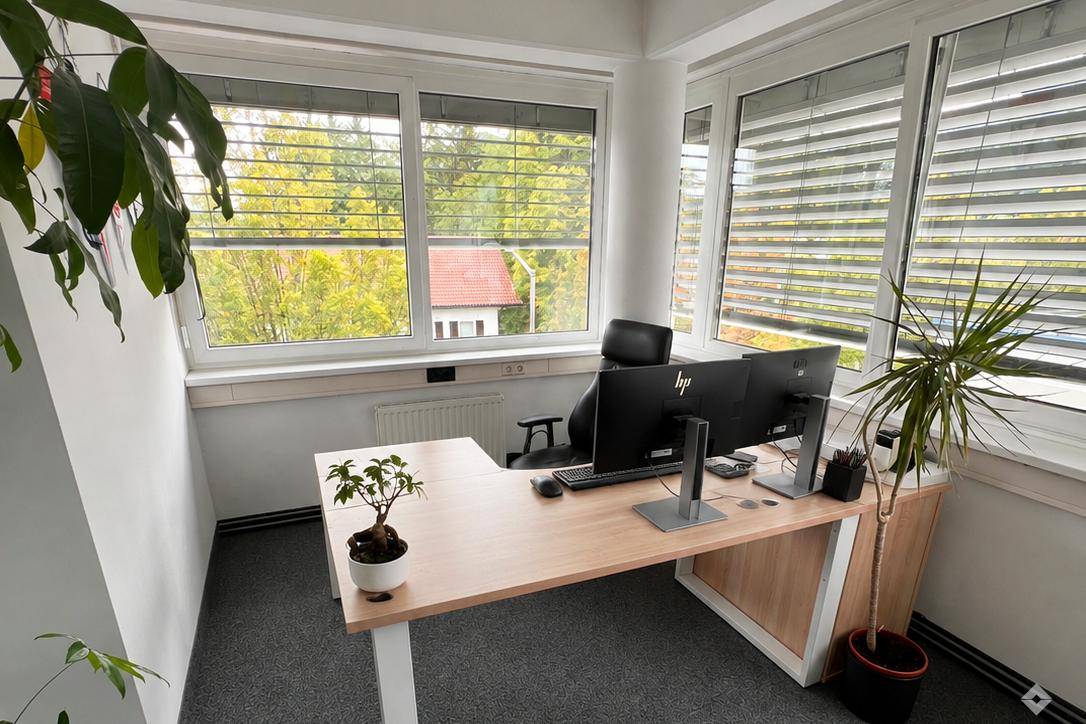 Modern eingerichtetes Büro mit Schreibtisch, Computermonitoren und Blick ins Grüne durch große Fenster.
