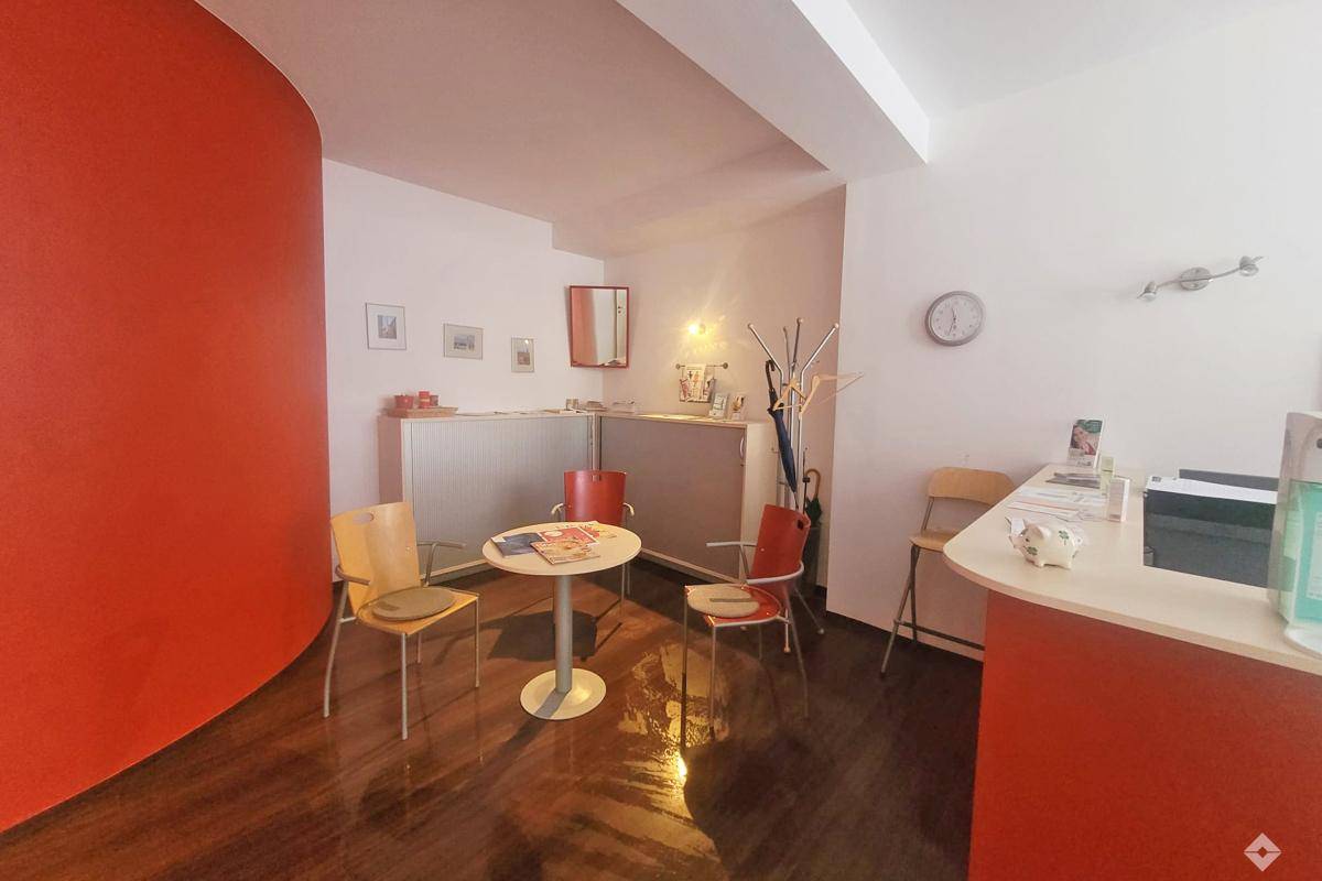 Heller Empfangsbereich mit roter Akzentwand, Holzboden und Sitzgelegenheiten für Besucher.