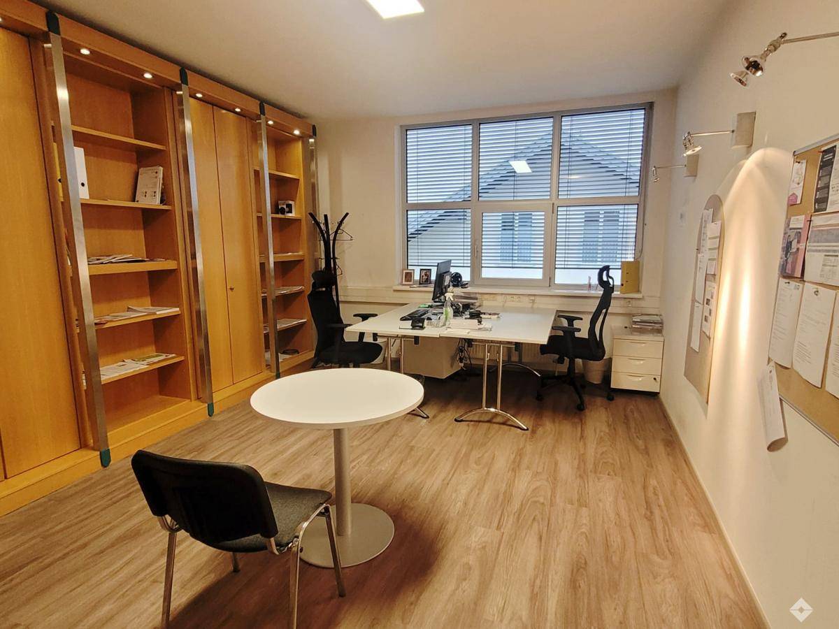 Geräumiges Büro mit Besprechungsecke, großen Fenstern und hellem Laminatboden, ideal für Teamarbeit.