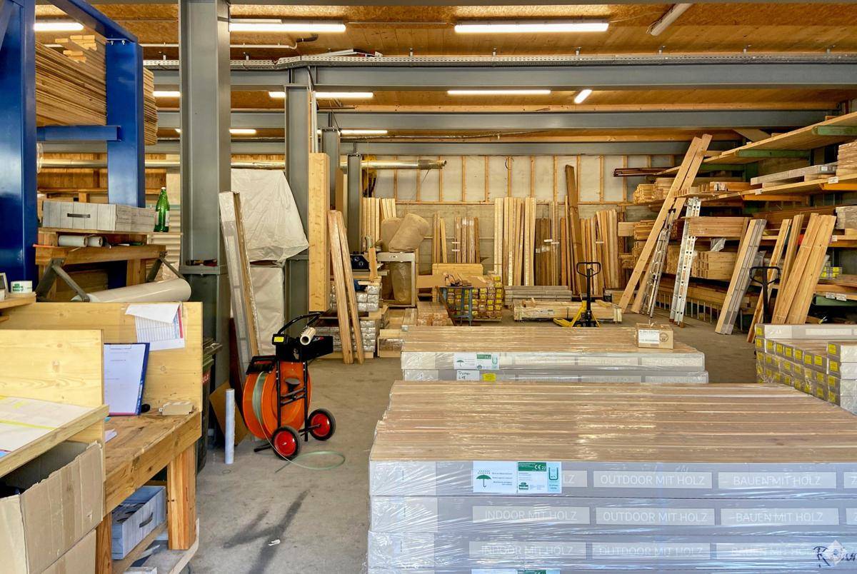 Lagerhalle mit gestapelten Holz- und Baumaterialien, gekennzeichnet durch Metallträger und hohe Decken.