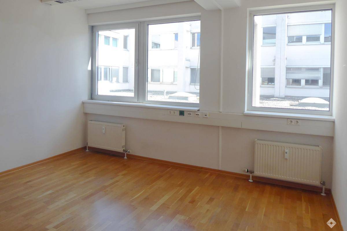 Geräumiger Büroraum mit mehreren Fenstern, Holzfußboden und Heizkörpern an der Wand.