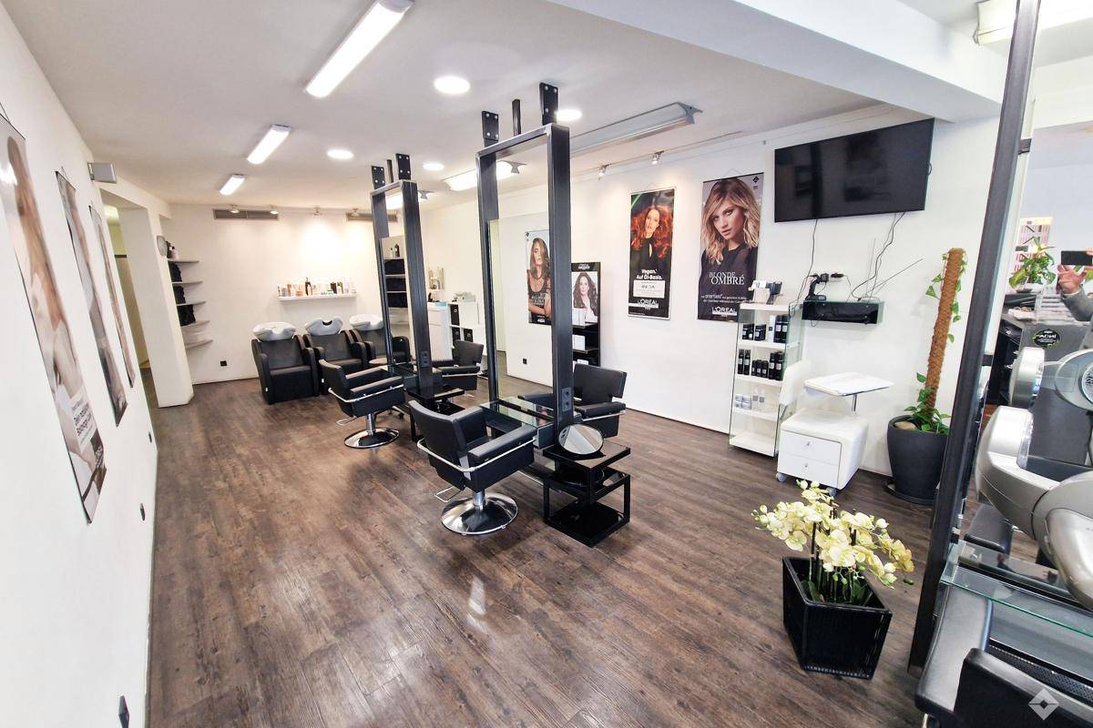 Heller Friseursalon mit modernen Styling-Stationen, großen Spiegeln und dunklem Holzboden.
