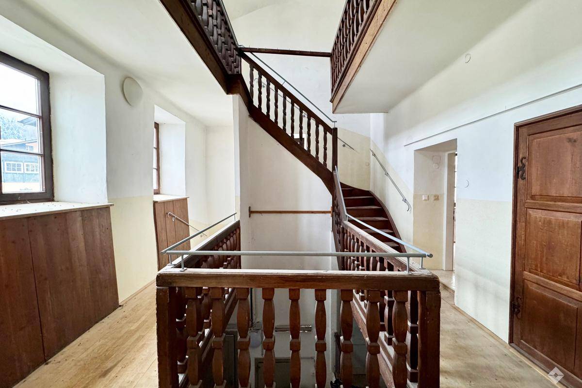 Historisches Treppenhaus mit Holzgeländer und hohen Decken, das den Charme des Altbaus bewahrt.
