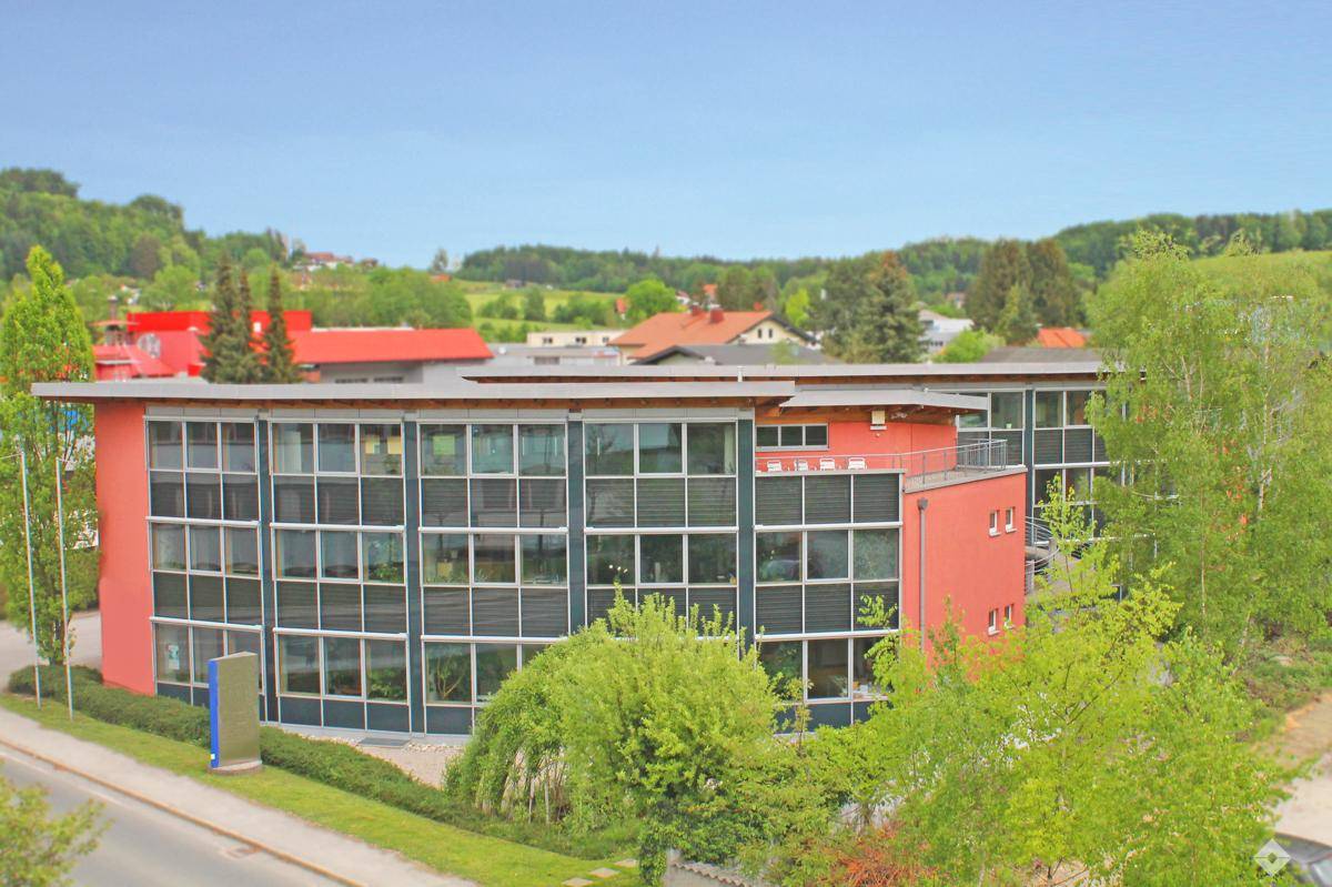 Modernes Geschäftsgebäude mit markanter roter Fassade und großen Fensterfronten in grüner Umgebung.