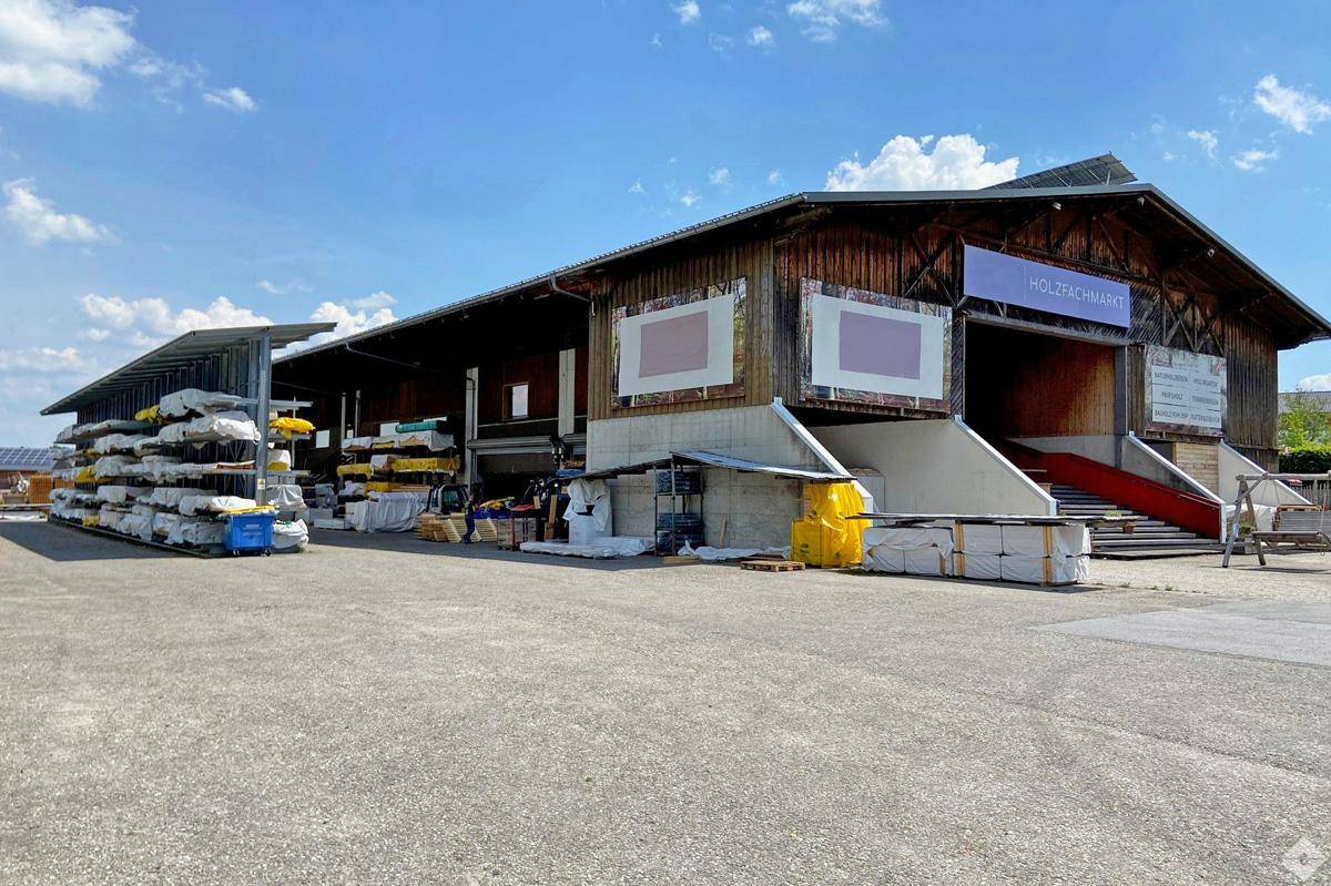 Großes Holzgebäude mit Lagerflächen im Freien und einem Schild für einen Holzfachmarkt.