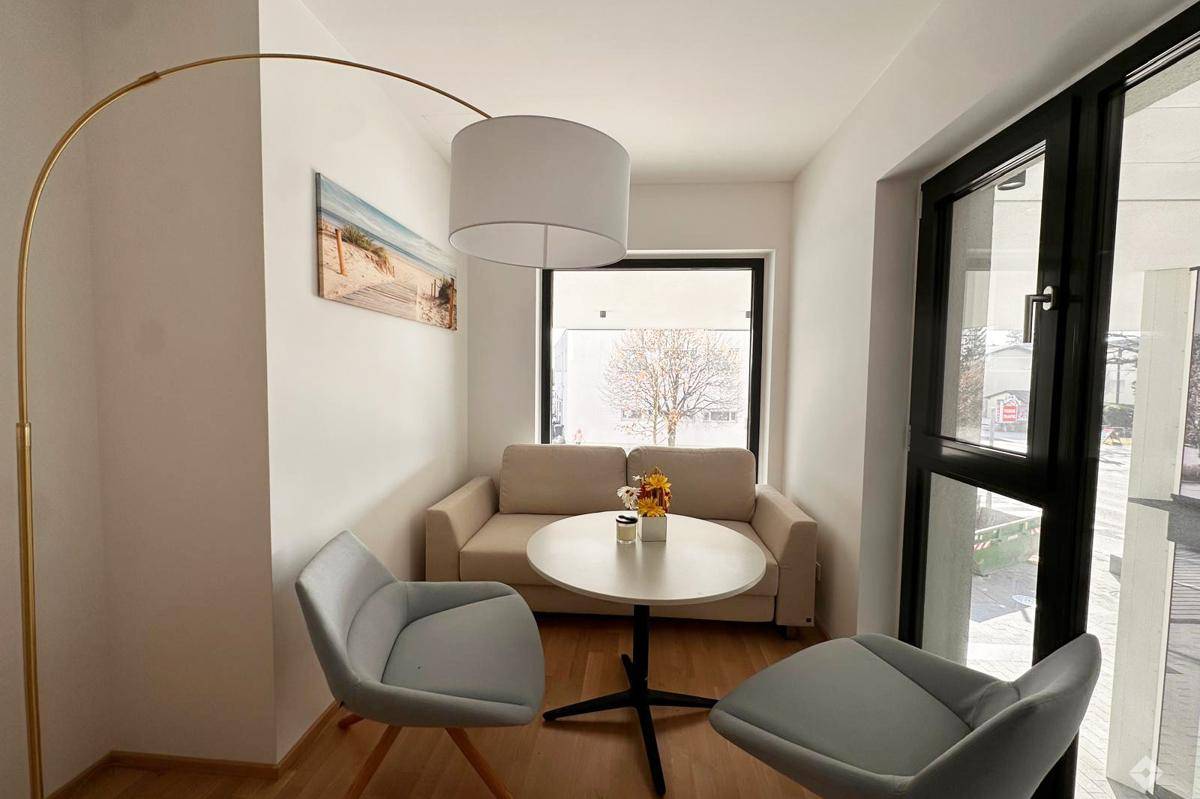 Gemütlicher Wohnbereich mit beigem Sofa, modernem Beistelltisch und Bogenlampe, hell durch große Fenster.