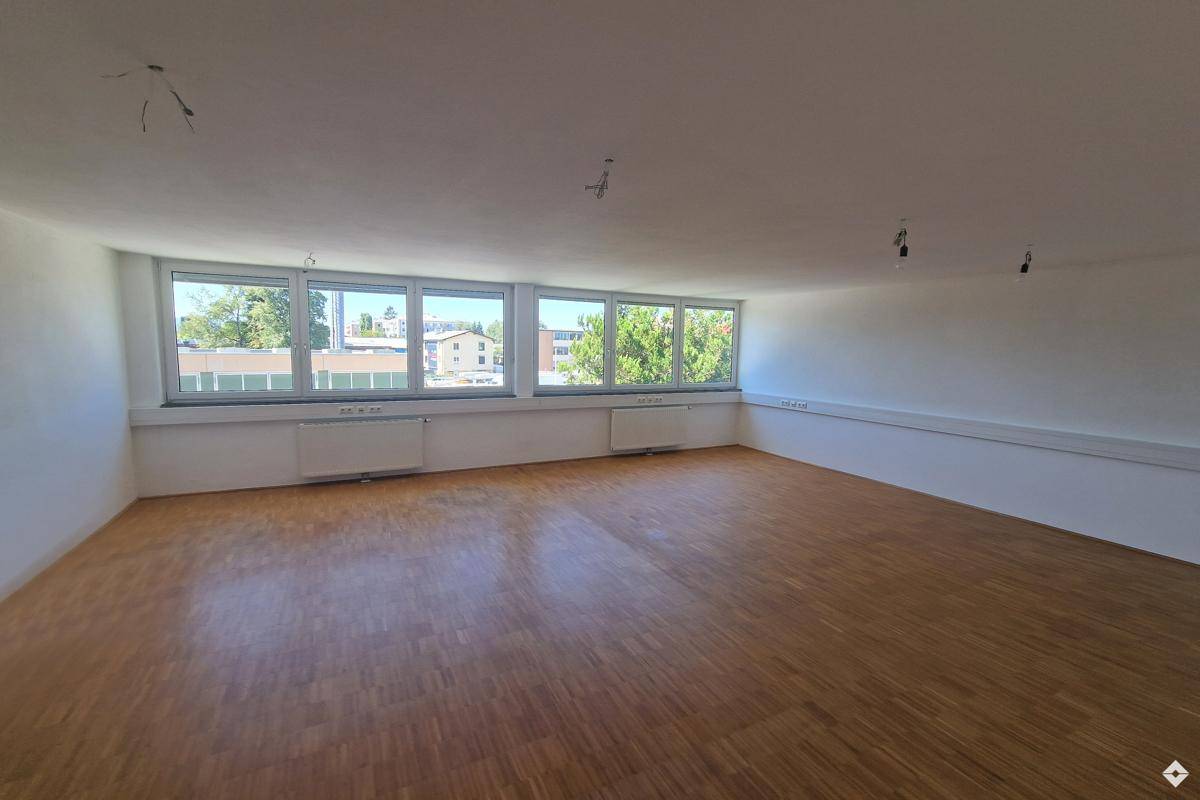 Geräumiger, heller Büroraum mit großen Fenstern und Holzboden, ideal für verschiedene Nutzungen.