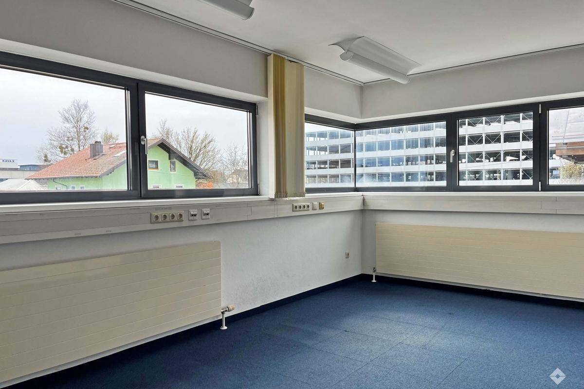 Geräumiges Büro mit weitem Ausblick, blauem Teppichboden und viel Tageslicht durch große Fenster.