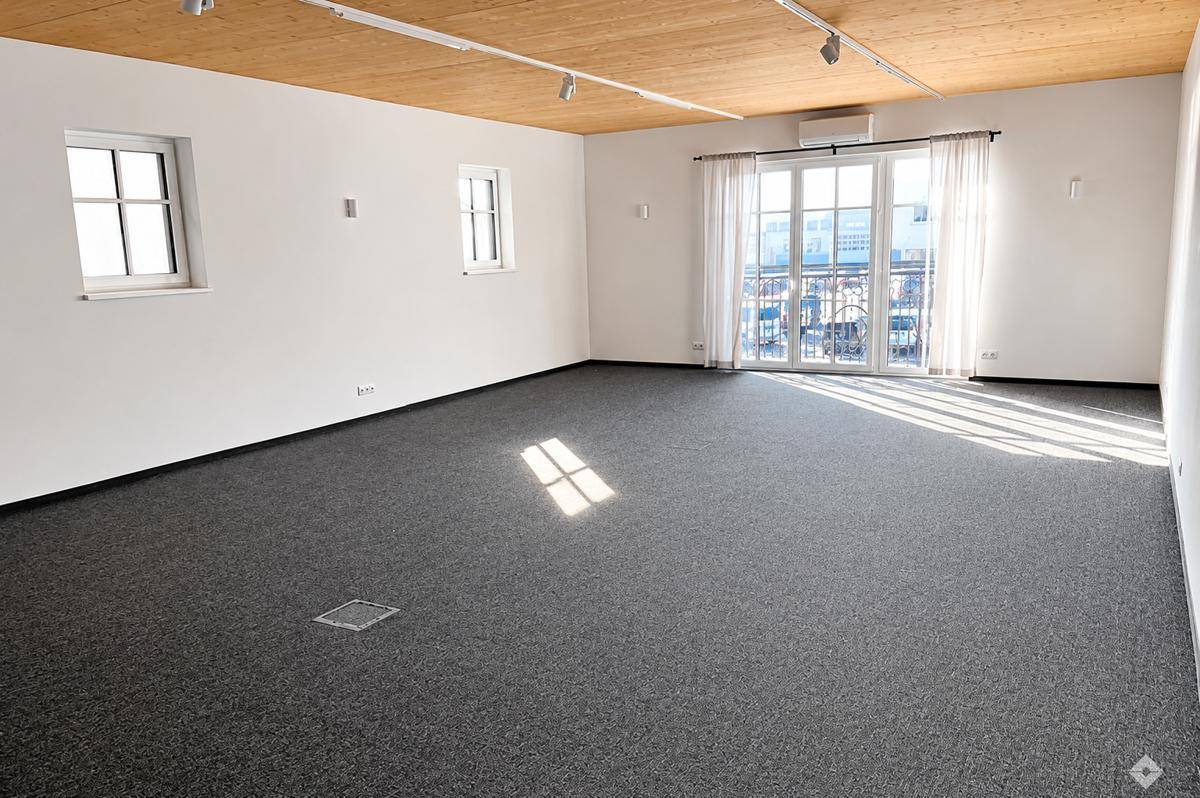 Geräumiger, heller Raum mit Teppichboden, Holzbalkendecke und Zugang zu einem Balkon.