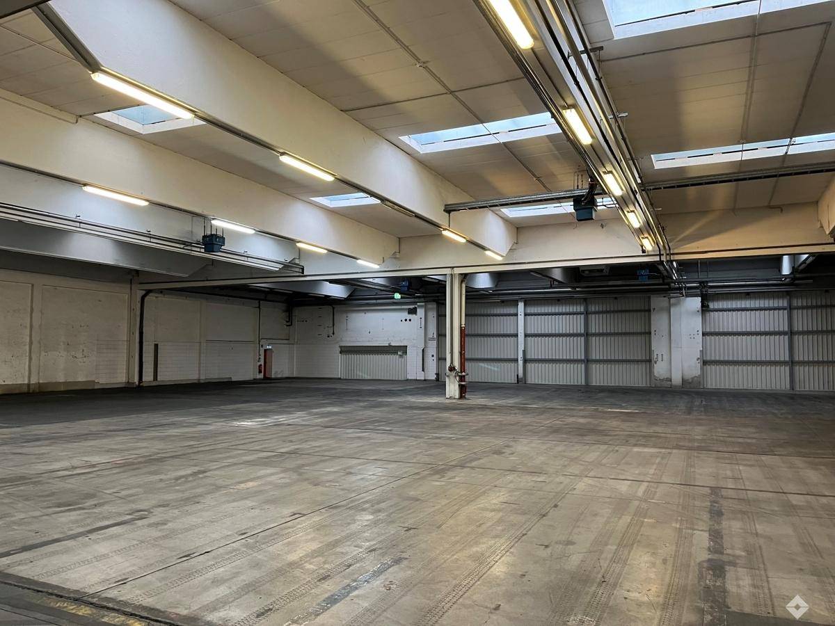 Geräumige, leere Industriehalle mit Betonboden, hohen Decken und Oberlichtern, ideal für Lagerung oder Produktion.