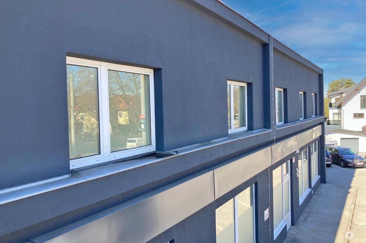 Leeres Büro mit Fischgrätparkett, weißen Wänden und einem großen Fenster, das viel Tageslicht hereinlässt.