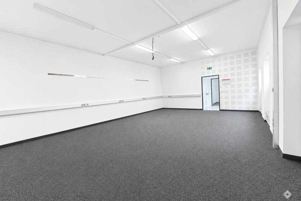 Flur mit Teppichboden, Übergang zu Steinfliesen und einer kleinen Küchenzeile im Hintergrund.