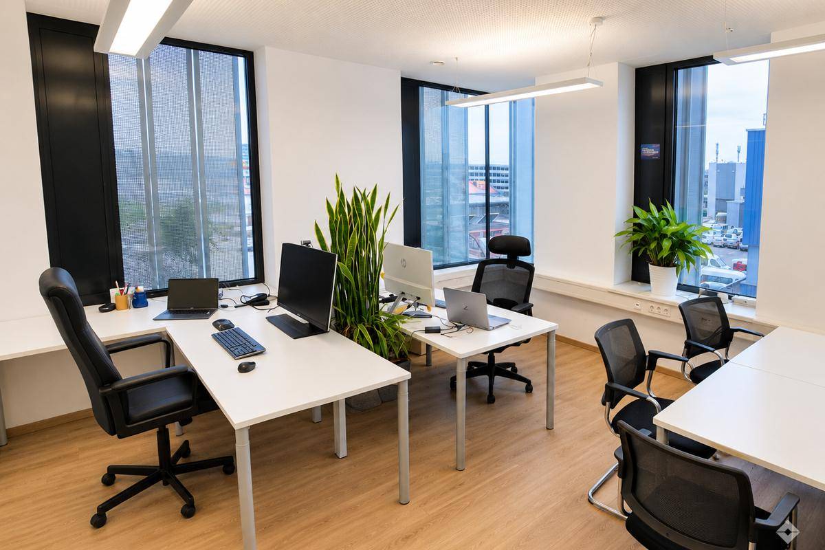 Modernes Großraumbüro mit mehreren Arbeitsplätzen, großen Fenstern und viel Tageslicht.