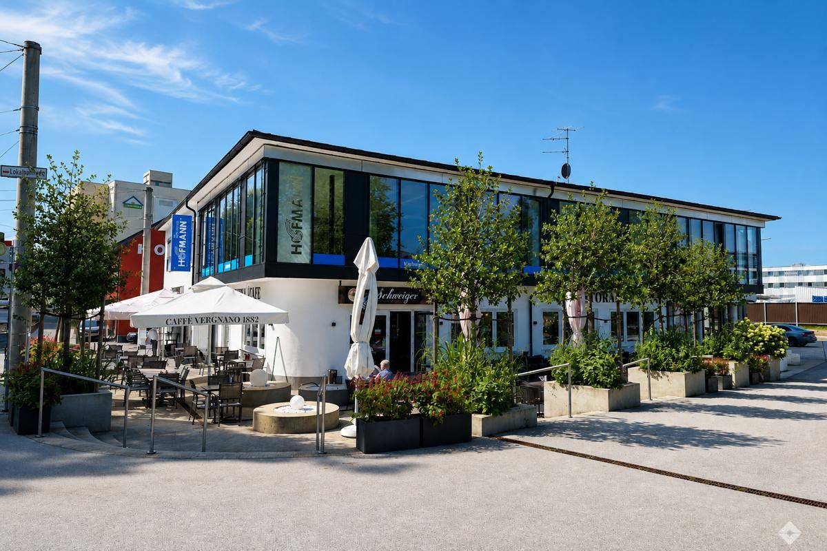 Modernes Geschäftsgebäude mit großen Glasfronten und einem Café mit Außenterrasse im Erdgeschoss.