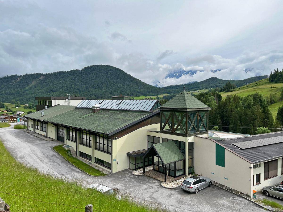 Gebäudeansicht mit markantem Eingangsbereich und umliegender Berglandschaft unter bewölktem Himmel.