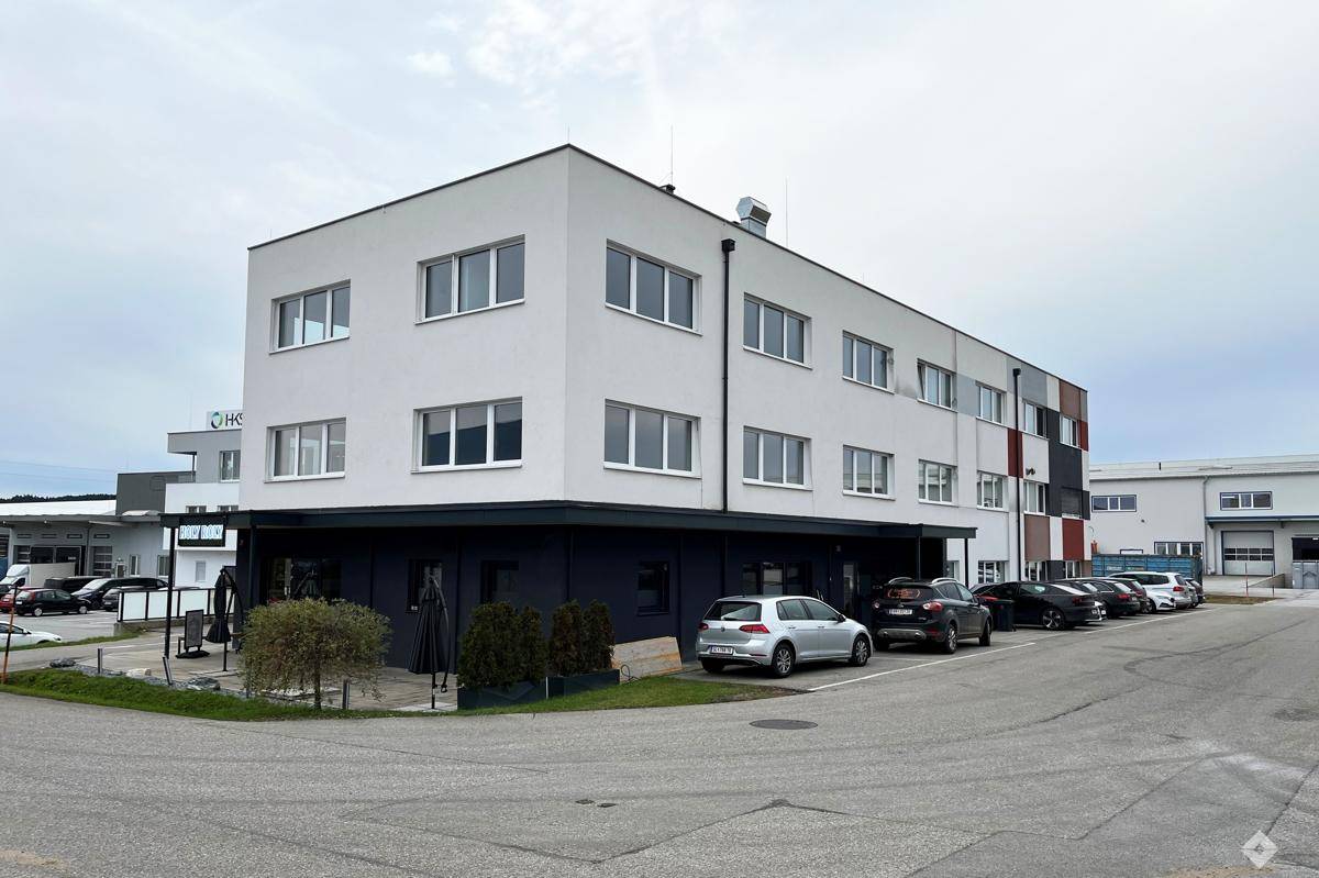 Gesamtansicht des modernen Geschäftsgebäudes mit Parkplätzen und umliegender Landschaft.