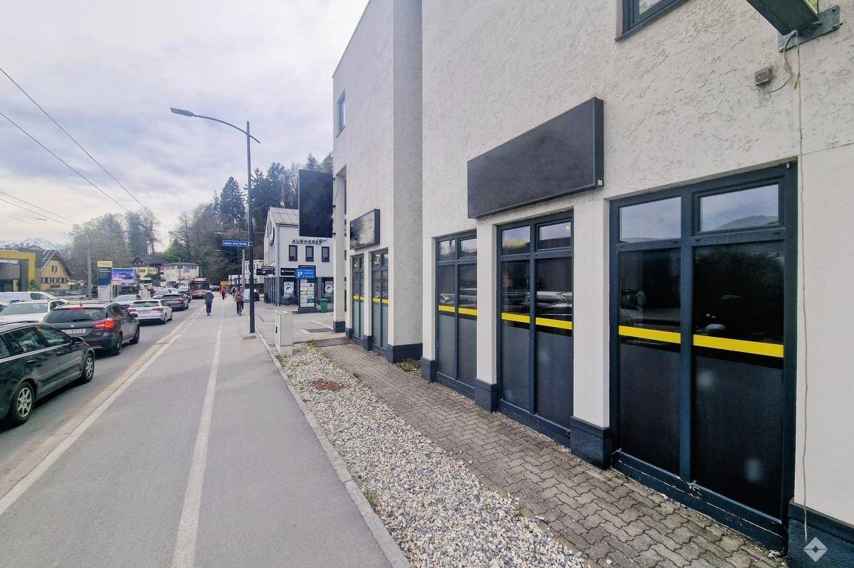 Blick auf die Geschäftsfassade entlang einer belebten Straße mit parkenden Autos und Fußgängern.