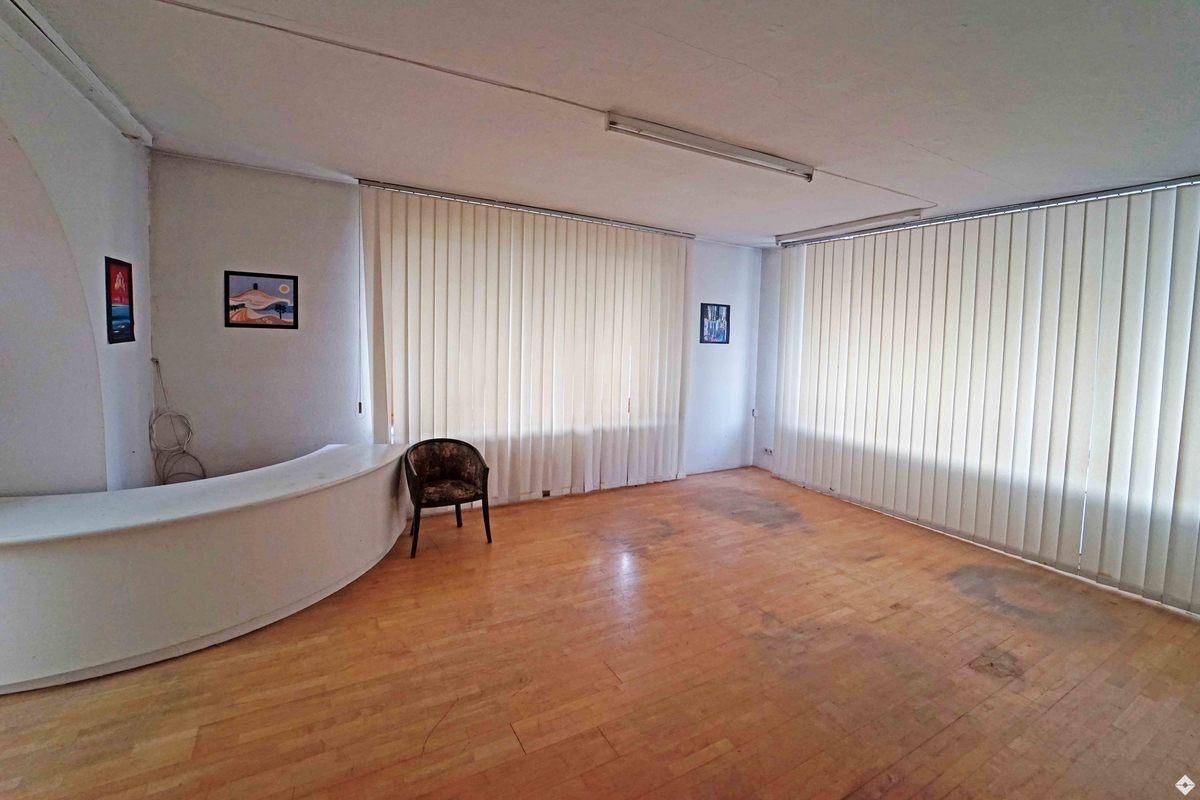 Heller Büroraum mit Holzparkettboden, einer geschwungenen Theke und großen Fenstern mit Jalousien.