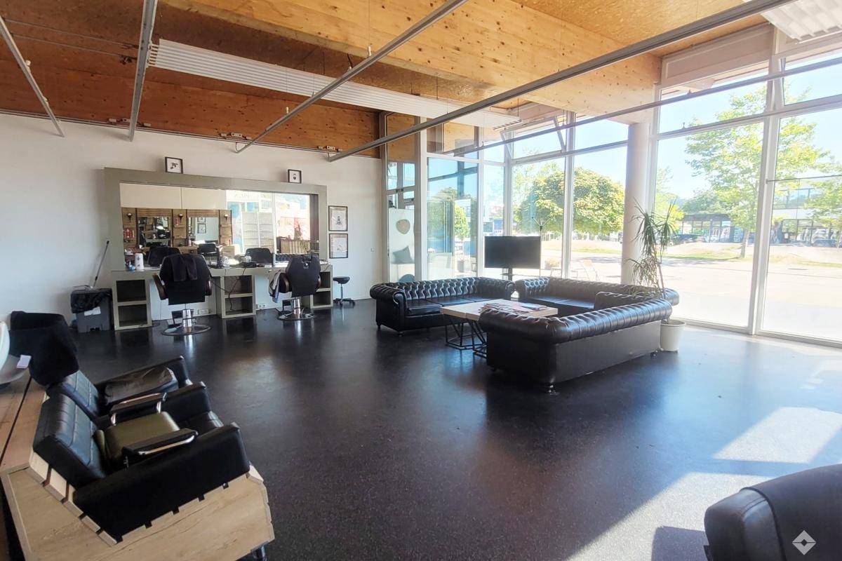 Moderner Friseursalon mit großen Spiegeln, dunklem Boden und einer einladenden Sitzecke, durchflutet von Tageslicht.