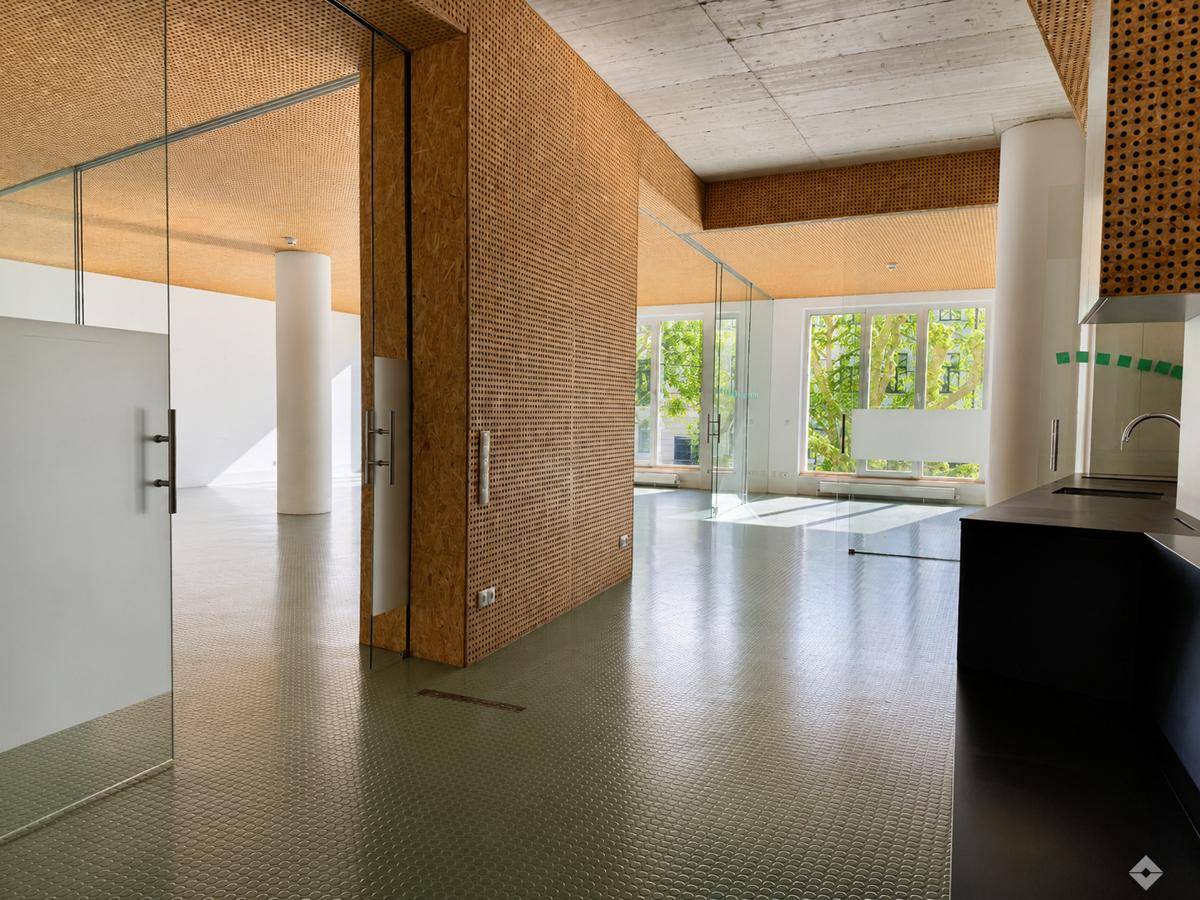Geräumiger, moderner Büroraum mit großen Fenstern, Glaswänden und einer kleinen Küchenzeile.