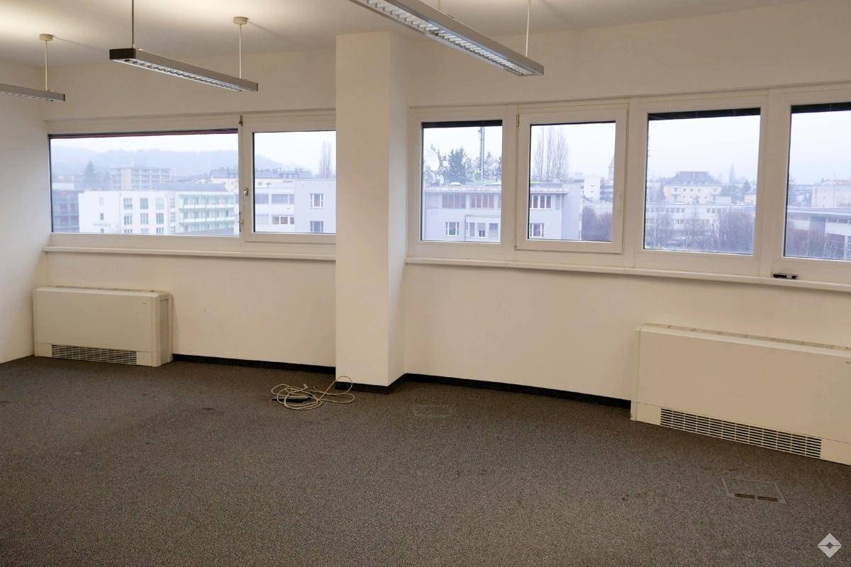 Heller Büroraum mit Teppichboden, großen Fenstern und Heizkörpern, bietet einen weiten Blick über die Stadt.